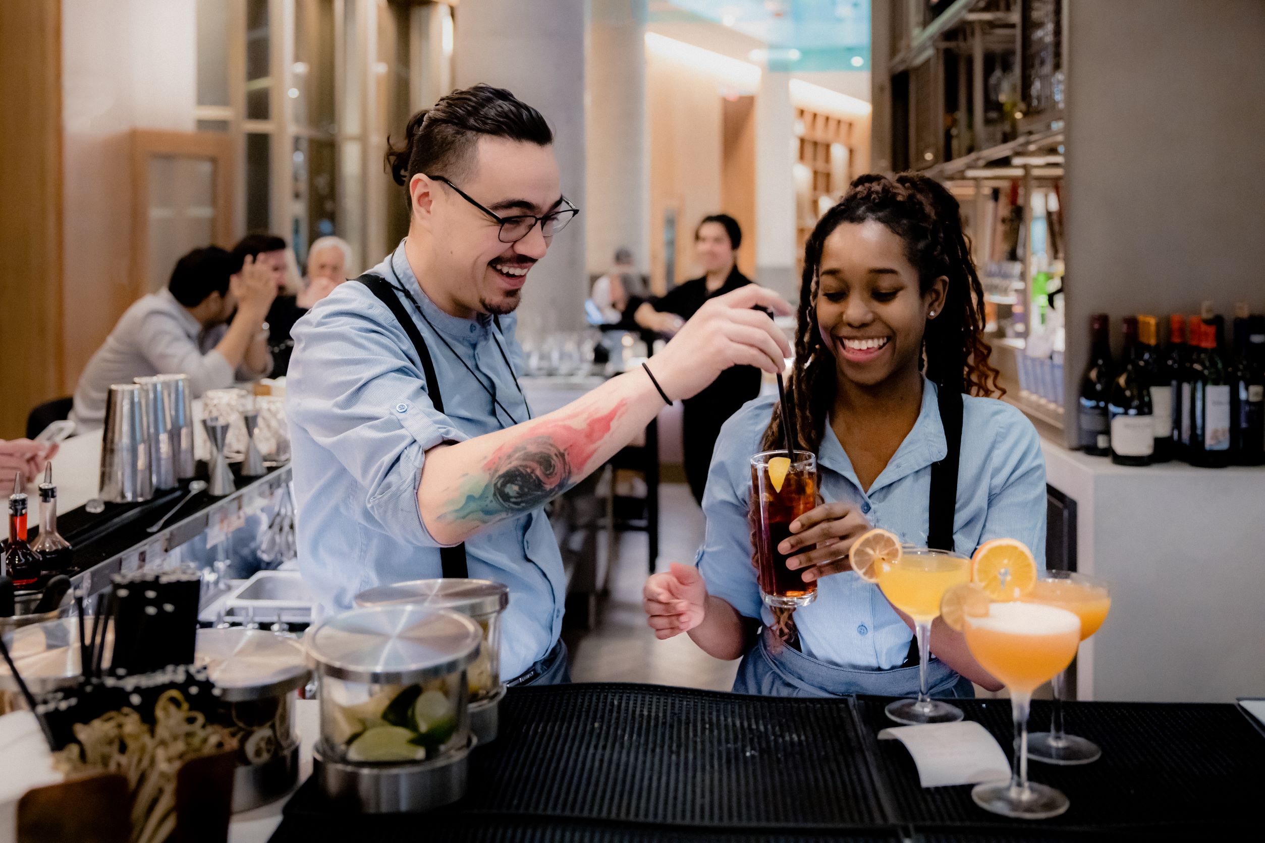 Two bartenders working on a cocktail behind a bar